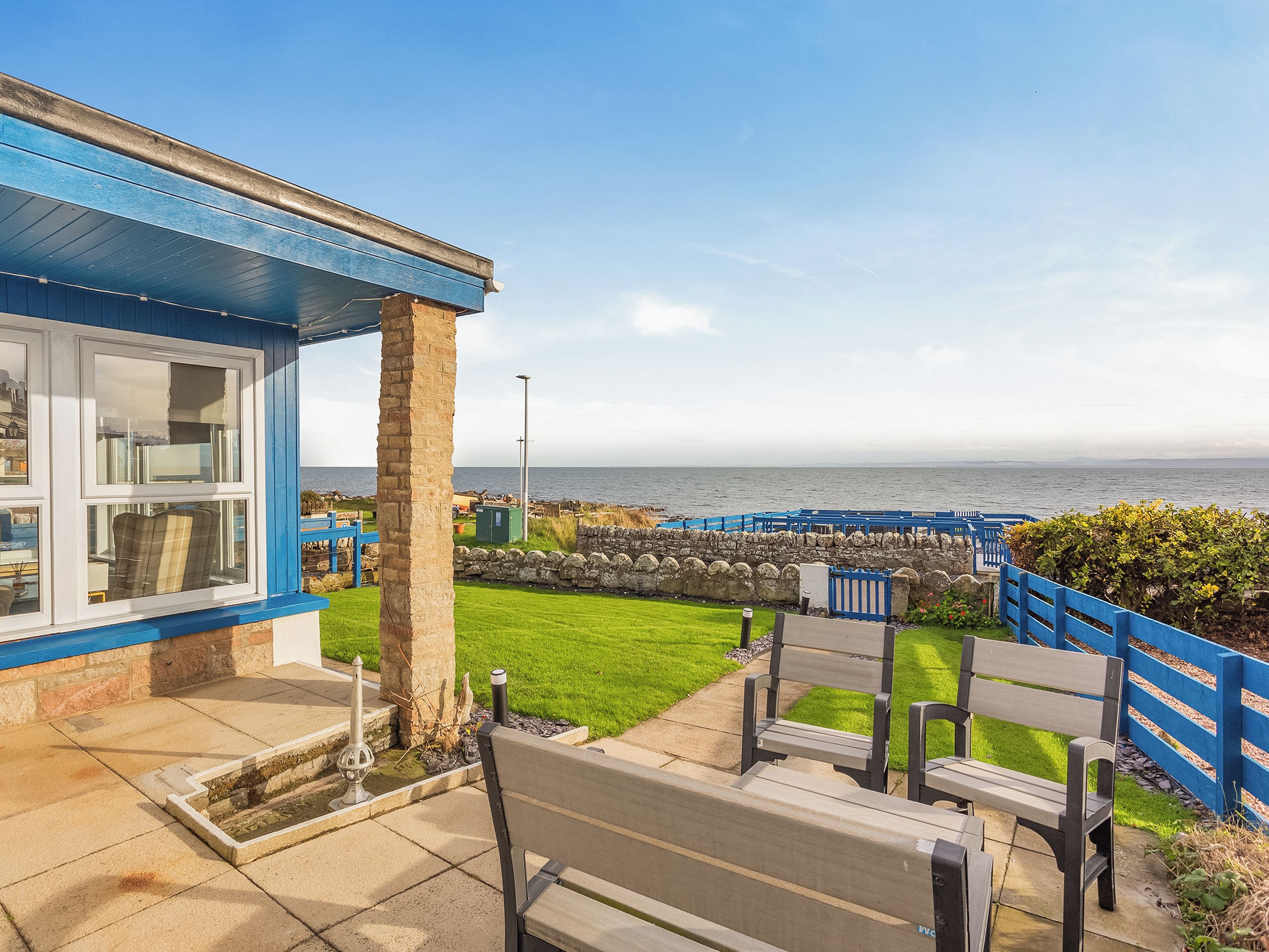 Un bâtiment situé sur la côte, avec une façade bleue, une zone herbeuse et un banc.