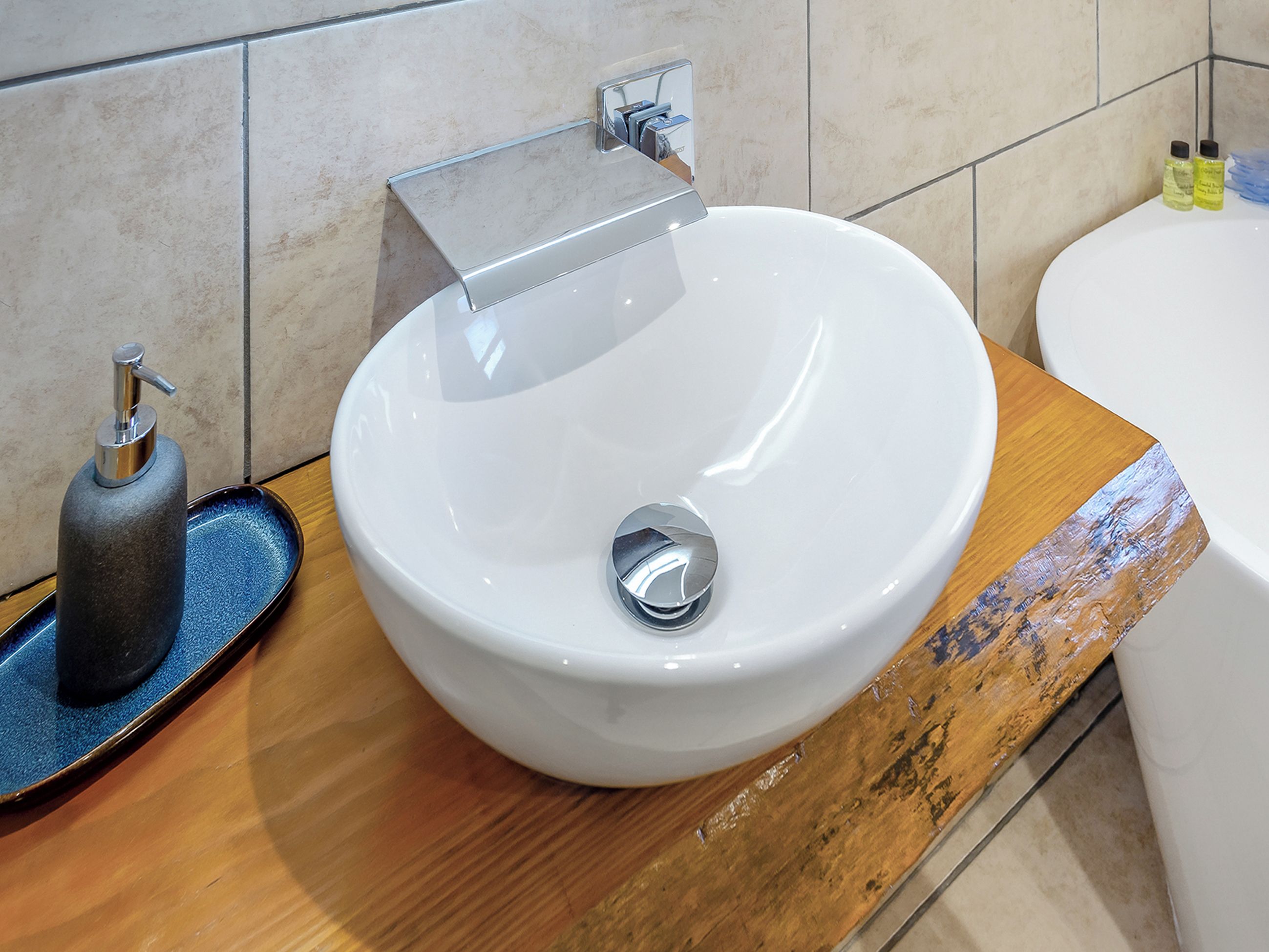 Een badkamer met een witte wastafel, een zeepdispenser en een kleine fles vloeibare zeep op het aanrecht.