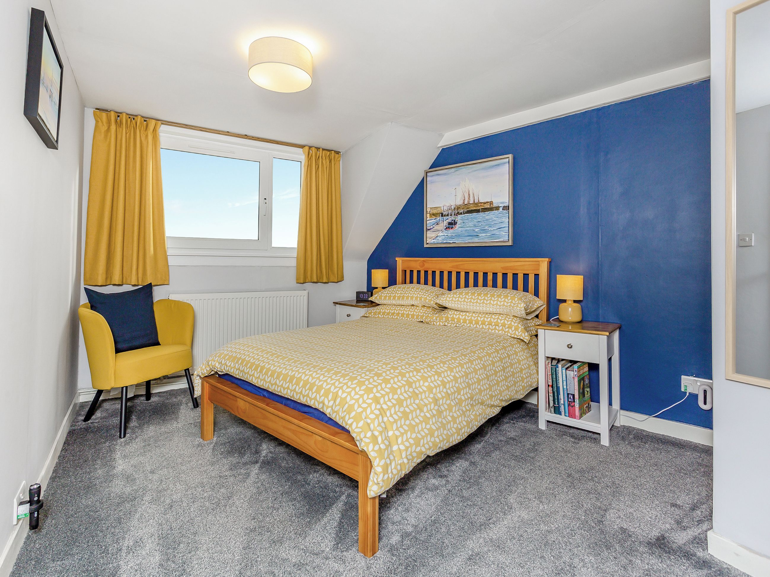 A bedroom with a bed, a chair, a nightstand, a lamp, a painting, and a window with curtains.