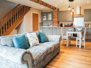 A living room with a sofa, a dining table, and a kitchen area with cabinets and a brick accent wall. - 1 bedroom accommodation in Skegness (Skegness)
