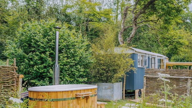 A wooden hot tub, a metal heater, and a small blue building in a garden setting. - UK41468 - Lapwing Hut (Cholderton, near Salisbury)