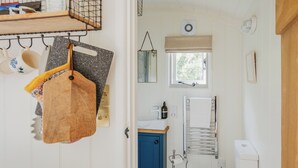 A compact bathroom with a white toilet, a blue cabinet, a towel rack, and a window with a view of trees. - UK41468 - Lapwing Hut (Cholderton, near Salisbury)