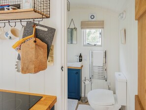 Ein kleines Badezimmer mit Toilette, blauem Schrank, Handtuchhalter und einem Fenster mit Blick auf Bäume.