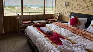 Ein Hotelzimmer mit Bett, einem Holzstuhl, einem kleinen Tisch und Blick auf Berge und einen See.