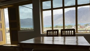 Ein Zimmer mit Holztisch und zwei Stühlen, große Fenster mit Blick auf Berge und ein Gewässer.