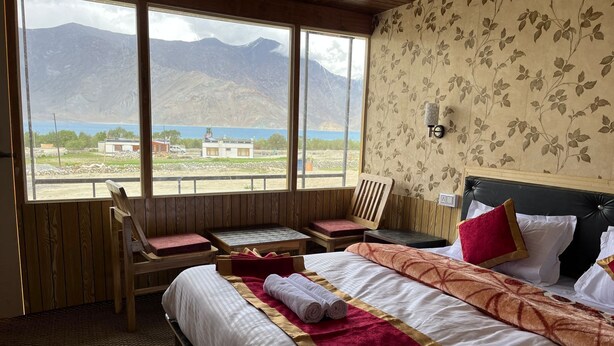 Ein Hotelzimmer mit Bett, einem Holzstuhl, einem kleinen Tisch und Blick auf Berge und einen See.