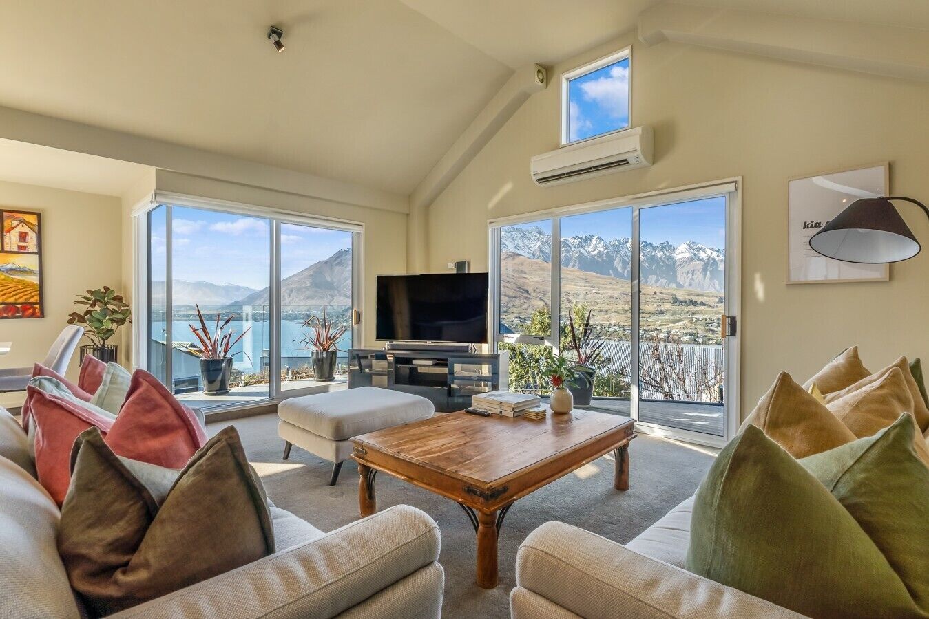 A spacious living room with a large flat-screen TV, comfortable seating, and a view of mountains through large windows.