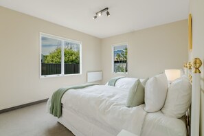 A bedroom with a bed, two windows, a radiator, and a lamp. - The Highview | Remarkables Panorama (Queenstown)