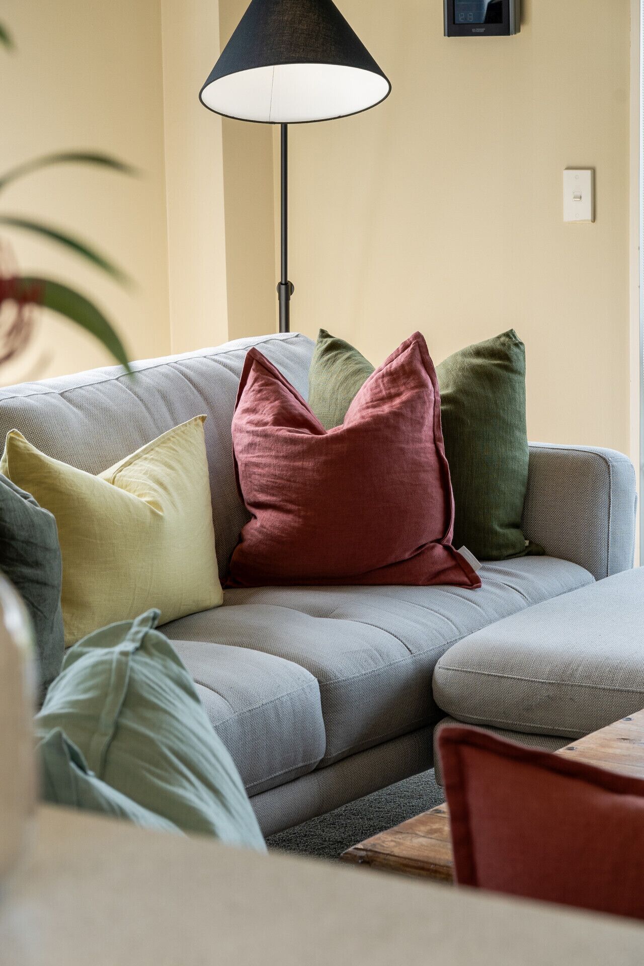 Un canapé gris agrémenté de plusieurs coussins de différentes couleurs, un lampadaire noir et une petite table avec une chaise.