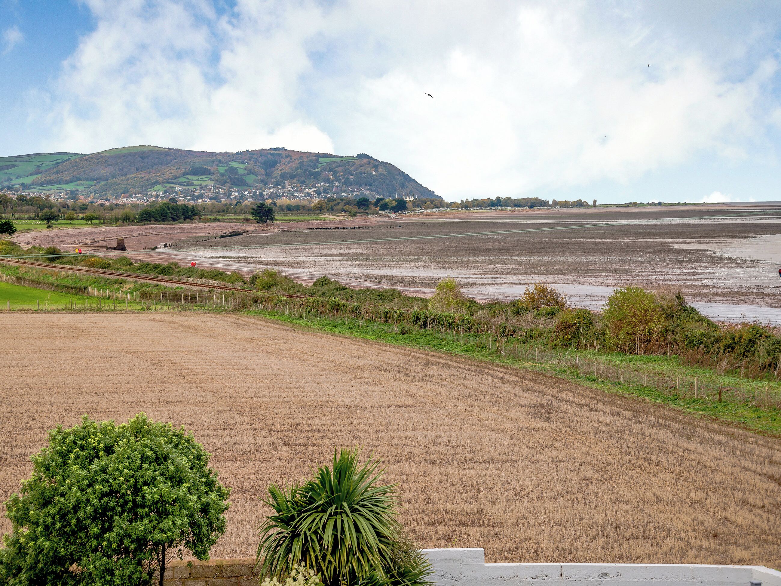A rural landscape with fields, a railway track, and a hill in the background.