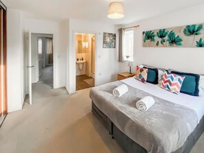 A hotel room with a large bed, a bedside table, a nightstand, a window with curtains, and a bathroom visible through an open door. - 4 bedroom accommodation in Ashford (Ashford)