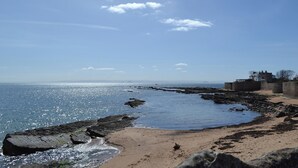 Eine Küstenlandschaft mit sandigem Strand, felsigem Ufer und blauem Himmel.