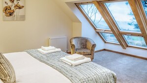 Ein Schlafzimmer mit schräg verlaufender Decke, einem Heizkörper, einem Sessel, einem Bett mit Kissen und einem Bild an der Wand.