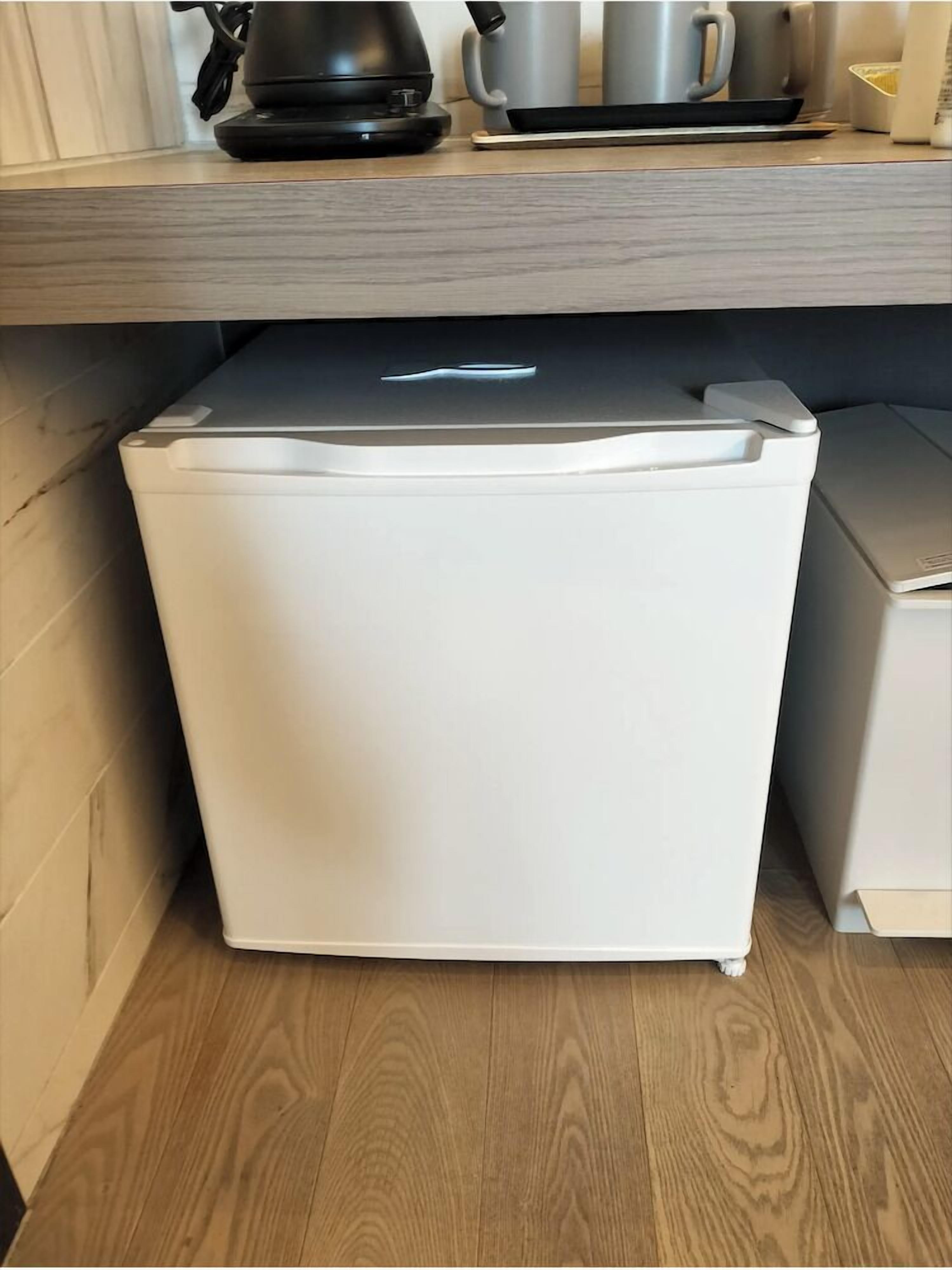 A compact white refrigerator in a kitchen with a wooden floor and a countertop above.