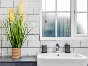 A bathroom with a white sink, two black soap dispensers, and a potted plant with green leaves and yellow flowers. - 3 bedroom accommodation in Ashford (Ashford)