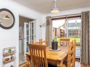 A dining area with a wooden table, chairs, a hanging light fixture, and a view of the backyard through a glass door. - 3 bedroom accommodation in Ashford (Ashford)