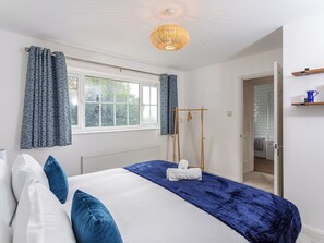 A bedroom with a large bed, a window with curtains, a wooden drying rack, and a bathroom visible through an open door. - 3 bedroom accommodation in Ashford (Ashford)