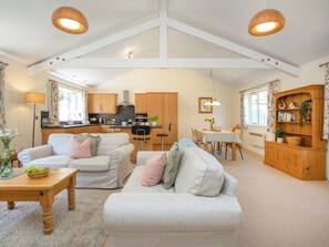 A spacious living area with a sofa, coffee table, and dining table. There is a kitchen with wooden cabinets and a dining area with a wooden cabinet and a plant. - Oaktree Cottage - HNNO (Bovey Tracey)