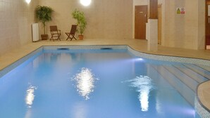 Piscina interna com paredes azulejadas, duas plantas em vasos e cadeiras de madeira.