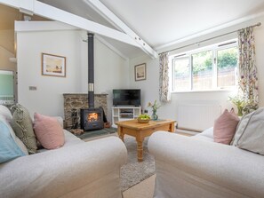 A living room with a fireplace, sofa, TV, and a window with curtains. - Oaktree Cottage - HNNO (Bovey Tracey)