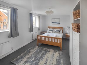A bedroom with a wooden bed, a grey and white rug, a white radiator, a window with curtains, and a wall-mounted lamp.