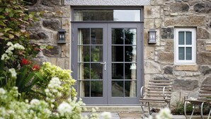 A stone building with a grey door, a small window, and a bench outside.