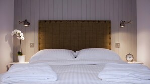 A neatly made bed with white linens, a wooden headboard, and two bedside lamps.