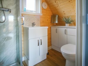 A bathroom with a shower, a sink, a toilet, and wooden walls.