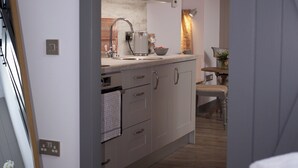 A modern kitchen with a sink, kettle, and a small table with a vase. - 1 bedroom accommodation in Oldmeldrum, near Inverurie (Oldmeldrum, near Inverurie)