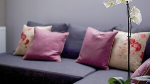 A modern living room with a grey sofa, purple and floral cushions, and a white orchid plant. - 1 bedroom accommodation in Oldmeldrum, near Inverurie (Oldmeldrum, near Inverurie)