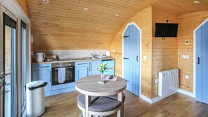 A wooden interior with a kitchen, a dining area, and a blue door. - A good sized, dog friendly pod with silent surroundings. (Archaracle)