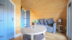 A wooden interior with a round table, grey sofa, and a vase with flowers. - A good sized, dog friendly pod with silent surroundings. (Archaracle)