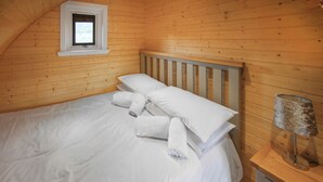 A wooden-paneled room with a bed, pillows, rolled towels, a lamp, and a small window. - A good sized, dog friendly pod with silent surroundings. (Archaracle)