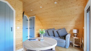 A wooden interior with a round table, grey sofa, and a lamp. - A good sized, dog friendly pod with silent surroundings. (Archaracle)