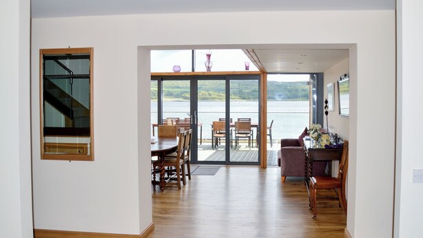 A spacious room with a wooden floor, a dining area with a table and chairs, and a large sliding glass door leading to a scenic outdoor view.