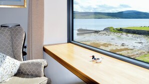 A room with a large window offering a view of a lake and mountains.