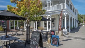 A white colonial-style building with a balcony, outdoor seating, and a sign indicating a bar is open. - Altitude Studio, one bedrooms studio in the heart of Martinborough (Martinborough)