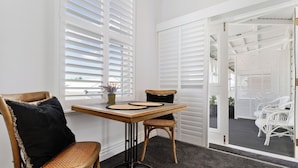 A dining area with a wooden table, two wicker chairs, and a black cushion. - Altitude Studio, one bedrooms studio in the heart of Martinborough (Martinborough)