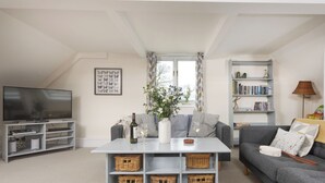 A living room with a TV, sofa, coffee table, and bookshelf. - 3 bedroom accommodation in Bovey Tracey (Bovey Tracey)