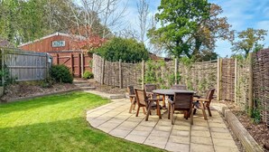 A patio with a round table and chairs, surrounded by a stone pathway and a wooden fence. - 3 bedroom accommodation in Bovey Tracey (Bovey Tracey)