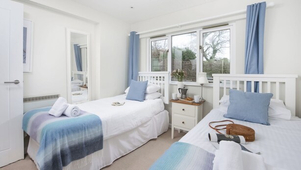 A bedroom with two beds, a bedside table, a mirror, and a window with curtains. - 3 bedroom accommodation in Bovey Tracey (Bovey Tracey)