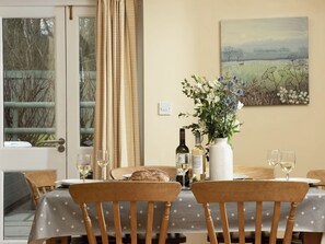 Een eethoek met een tafel gedekt voor twee personen, een vaas met bloemen, wijnflessen en een schilderij aan de muur.