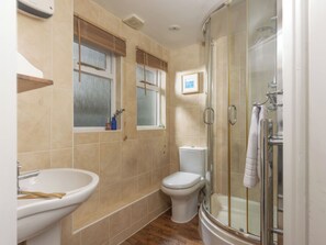 Een badkamer met douche, toilet, wastafel en raam met zonwering.