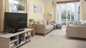 A living room with a television, two sofas, a coffee table, and a bookshelf. - 3 bedroom accommodation in Bovey Tracey (Bovey Tracey)