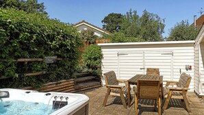 A hot tub, wooden table, and chairs in a backyard with a sign for a pool and games room. - 3 bedroom accommodation in Bovey Tracey (Bovey Tracey)