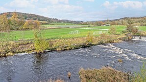 Een rivier die door een landelijk gebied stroomt, met velden en een verre heuvel.