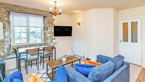 Ein Wohnzimmer mit Steinwand, einem Holzesstisch, blauen Sofas und einem an der Wand montierten Fernseher.