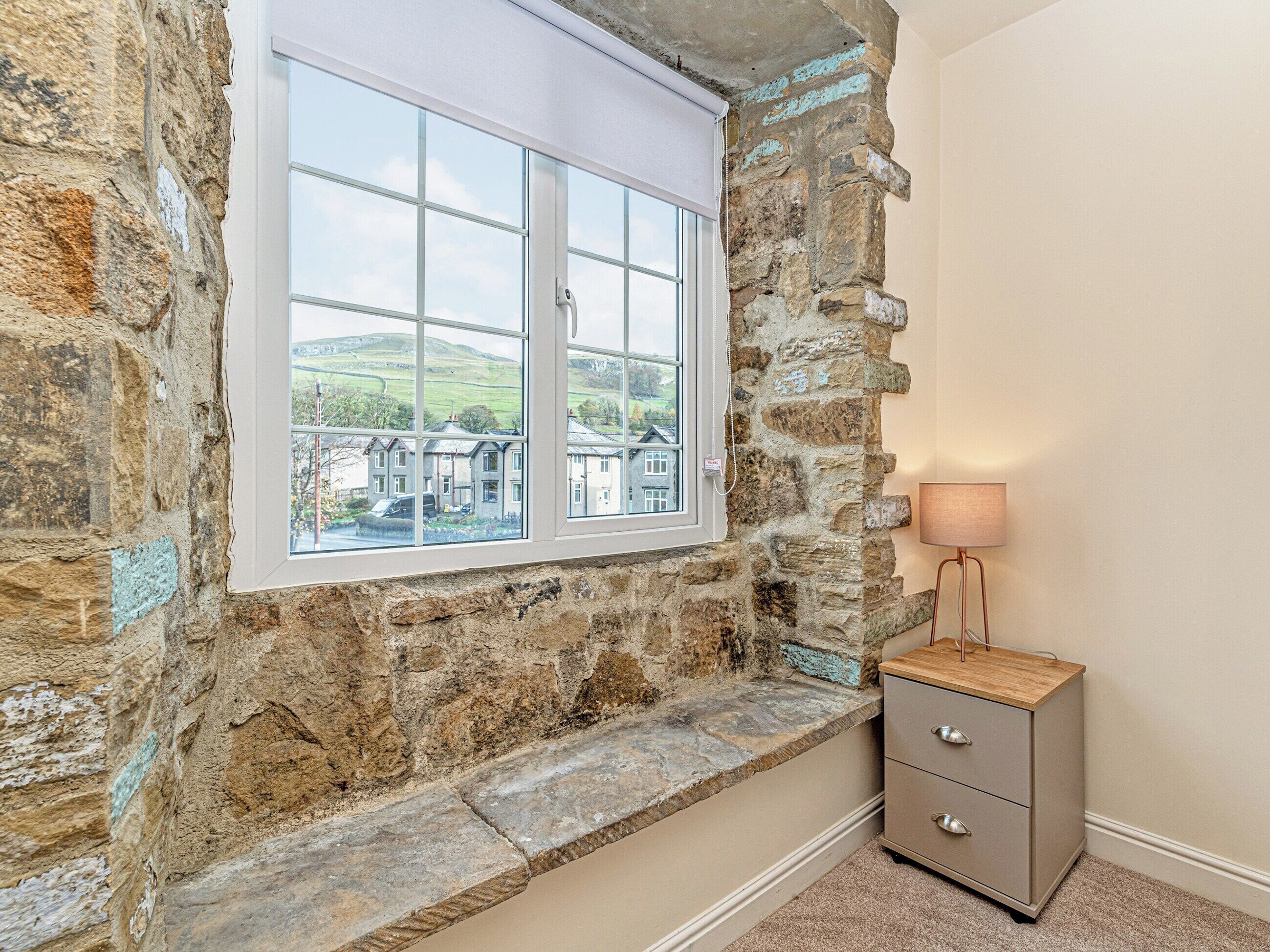 Quarto com paredes de pedra e janela com vista para uma área residencial.