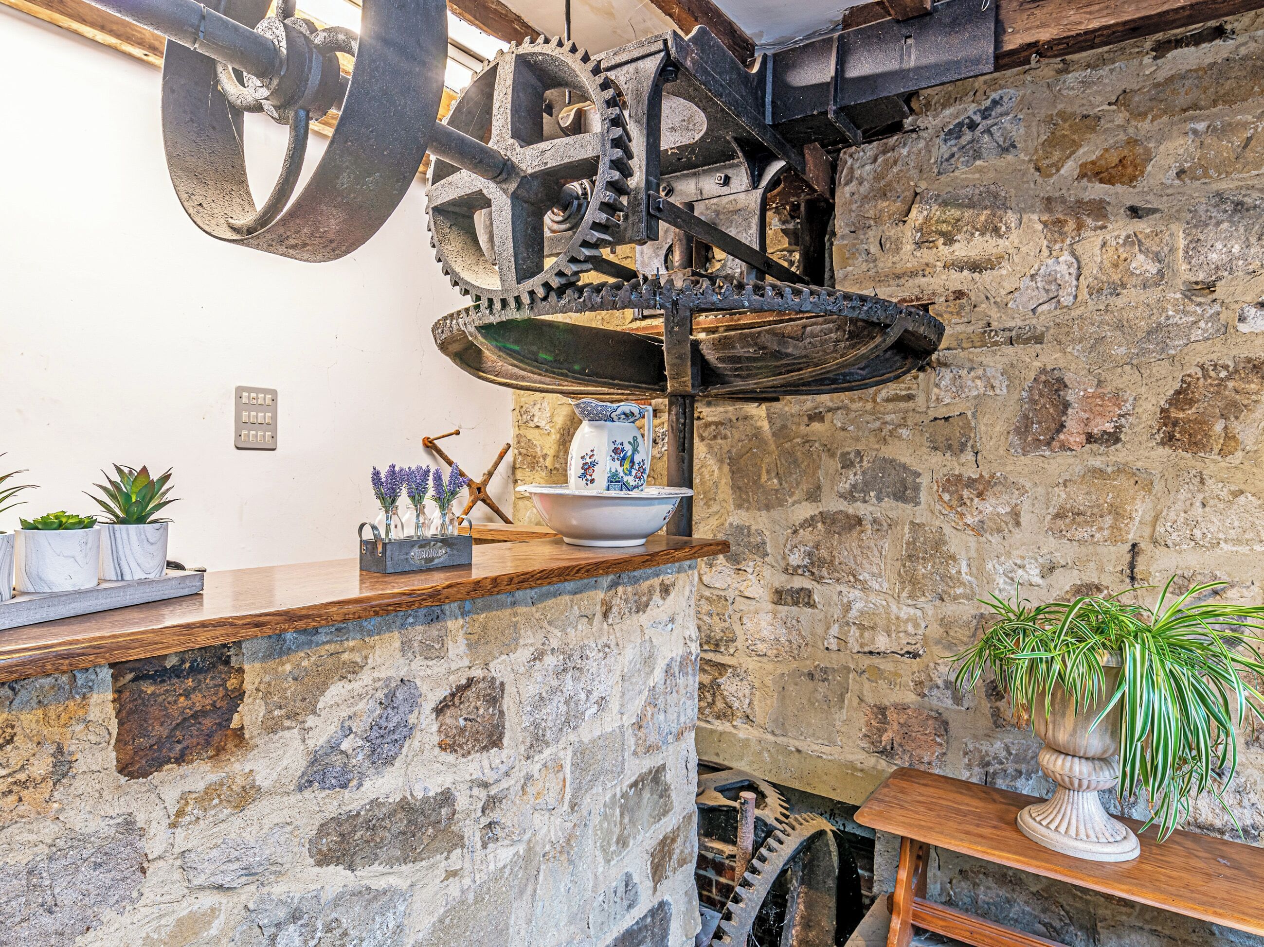 A rustic kitchen with exposed stone walls, a wooden counter, and a large mechanical gear.