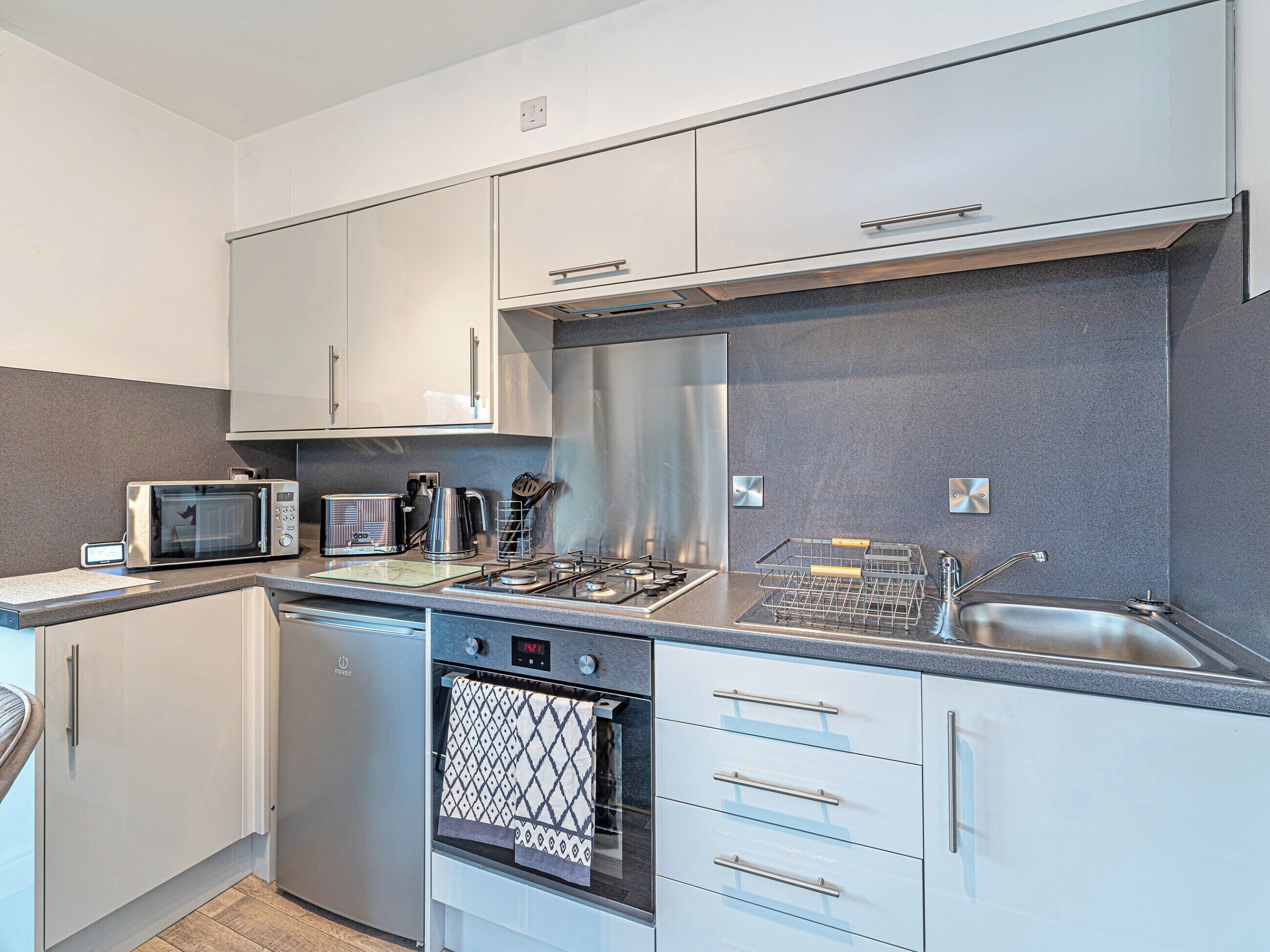 A modern kitchen with stainless steel appliances, white cabinetry, and a grey backsplash.
